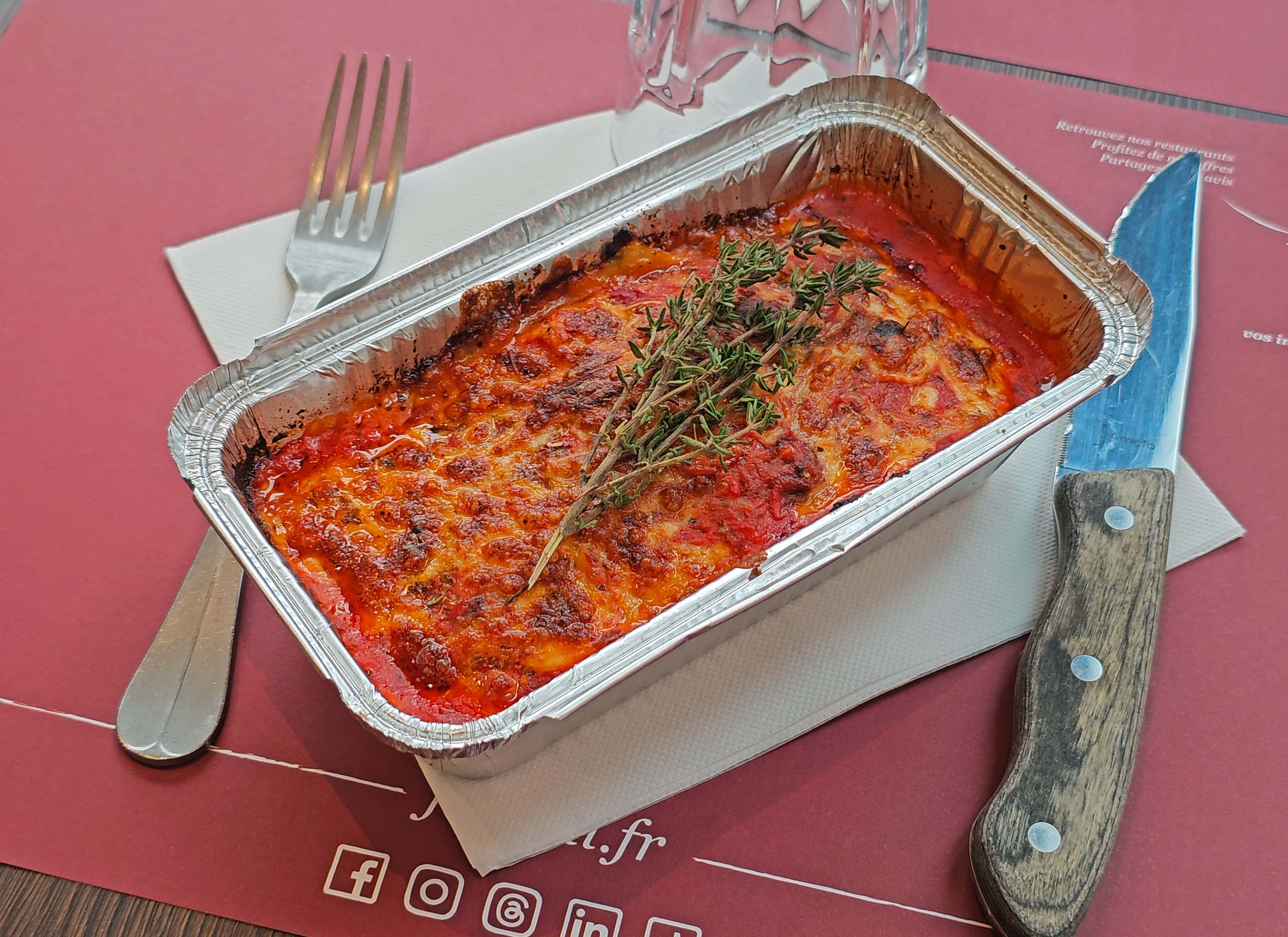Lasagne maison Fabioli gratinée dans sa barquette à emporter, garnie d'une branche de thym frais