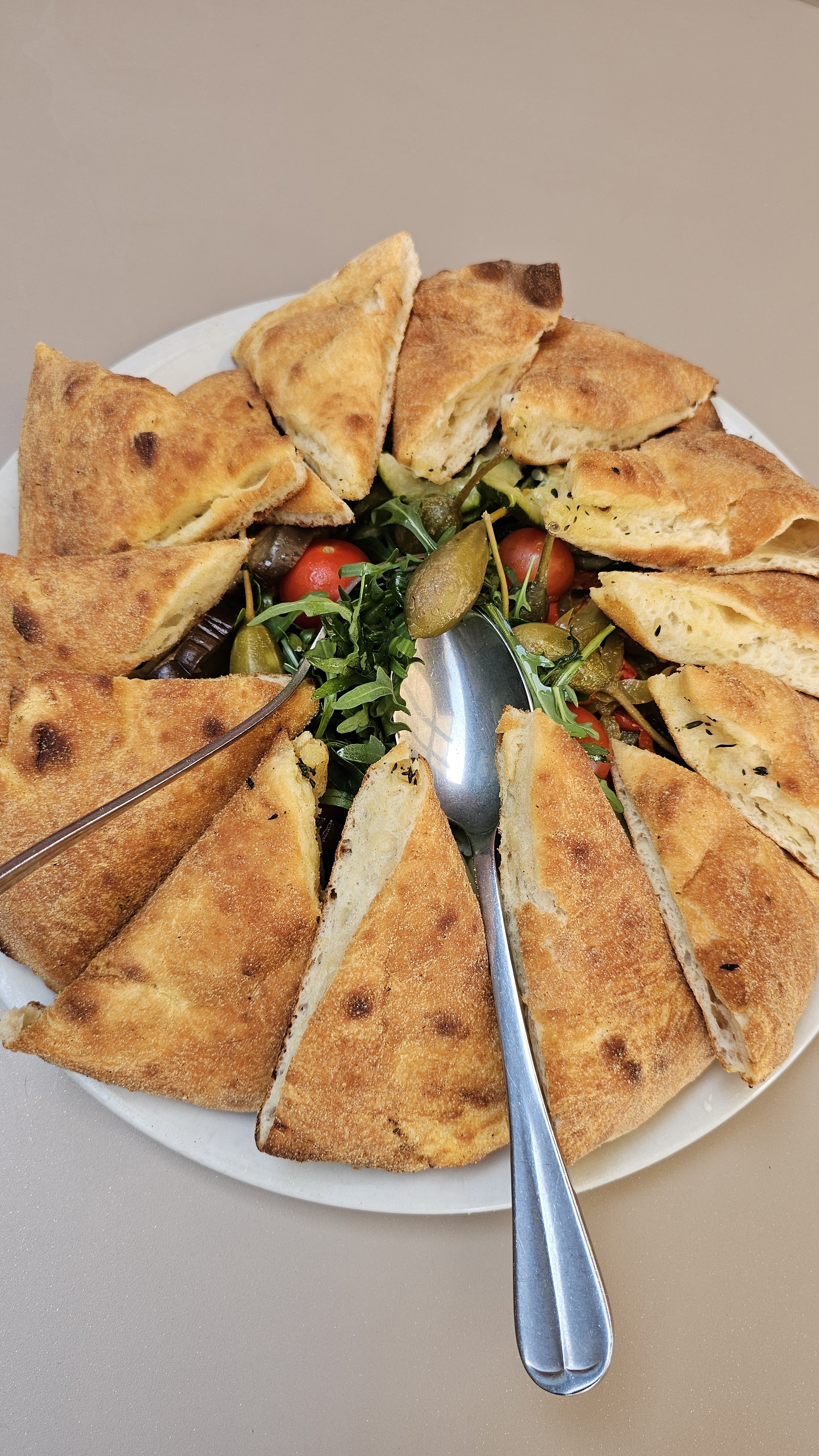 Pizza bianca della casa découpée en parts autour d'une salade de roquette, tomates cerises et câpres, chez Fabioli