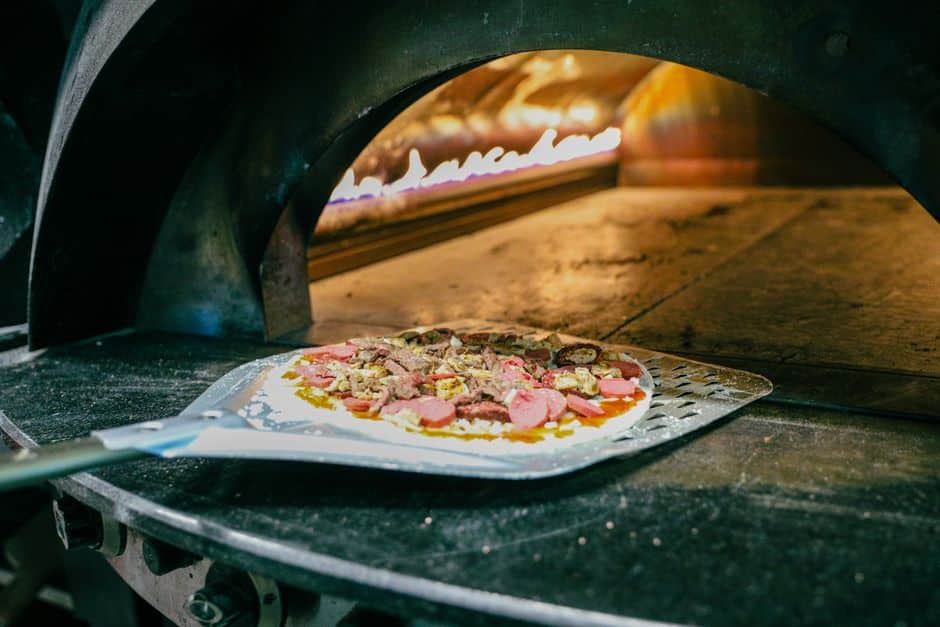 Pizza enfournée dans un four à bois traditionnel en pierre, flammes vives sur le côté