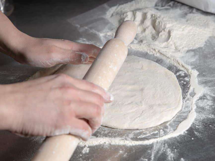 Mains de pizzaïolo étalant finement la pâte à pizza sur un plan fariné