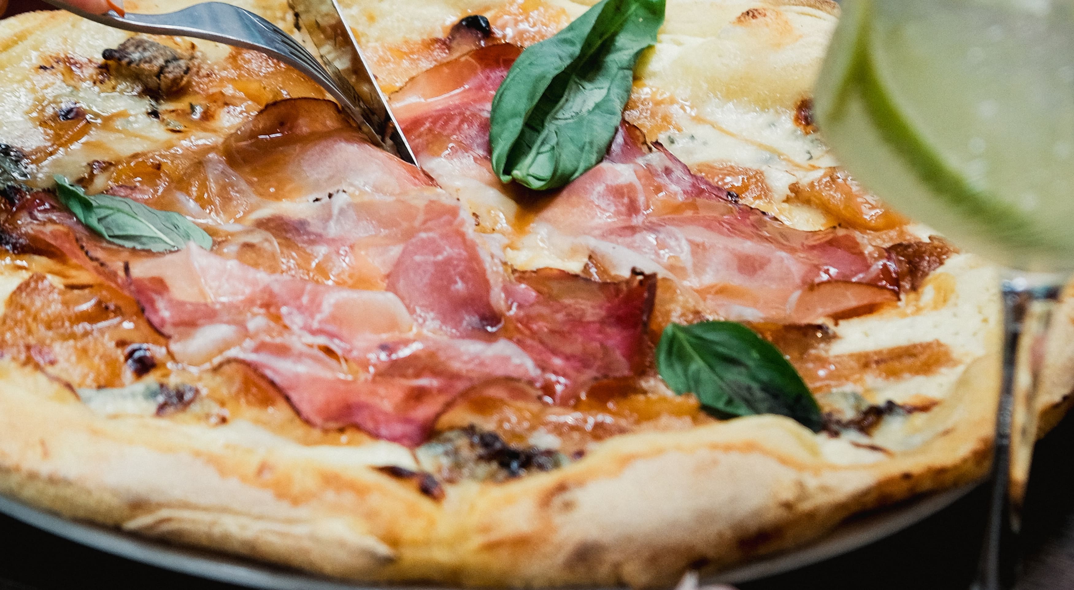 Gros plan d'une pizza au jambon cru et basilic frais, découpée à table chez Fabioli