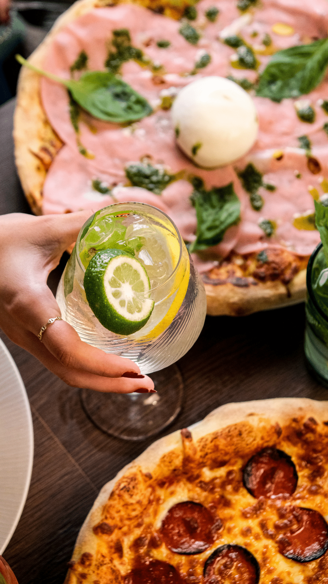 Spritz au citron vert levé au-dessus d'une pizza mortadelle burrata pesto et d'une pizza pepperoni
