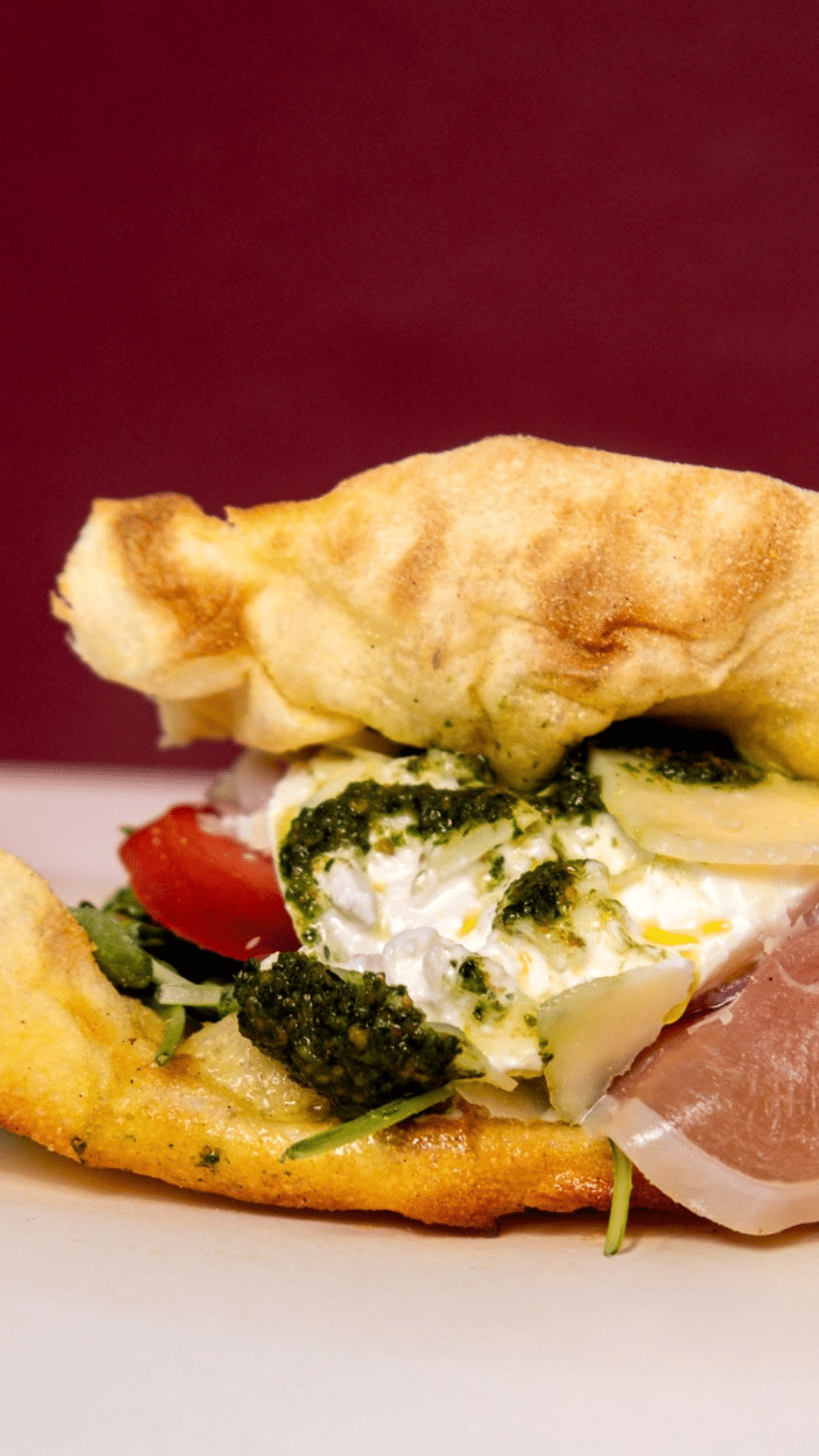 Panuozzo garni de burrata, pesto, tomate et jambon cru sur fond bordeaux