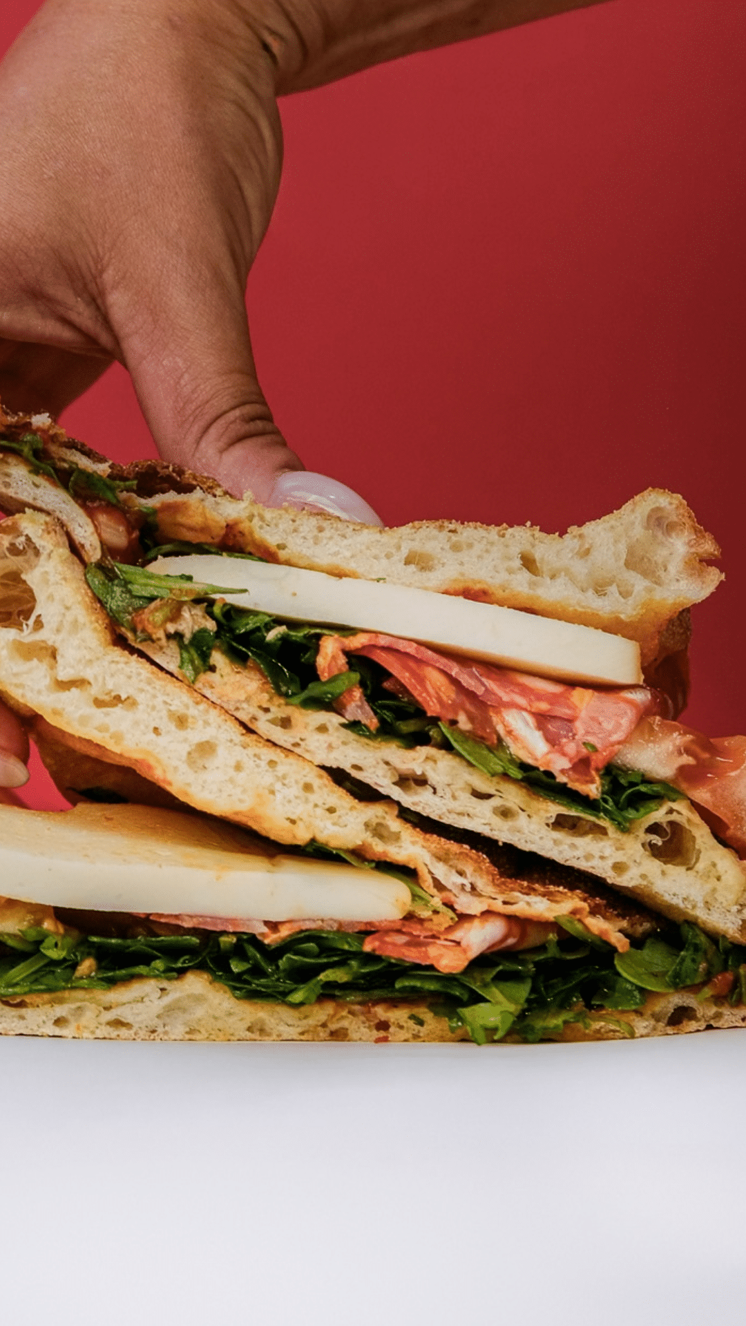 Main tenant des focaccias garnies de salami, fromage et roquette sur fond rouge