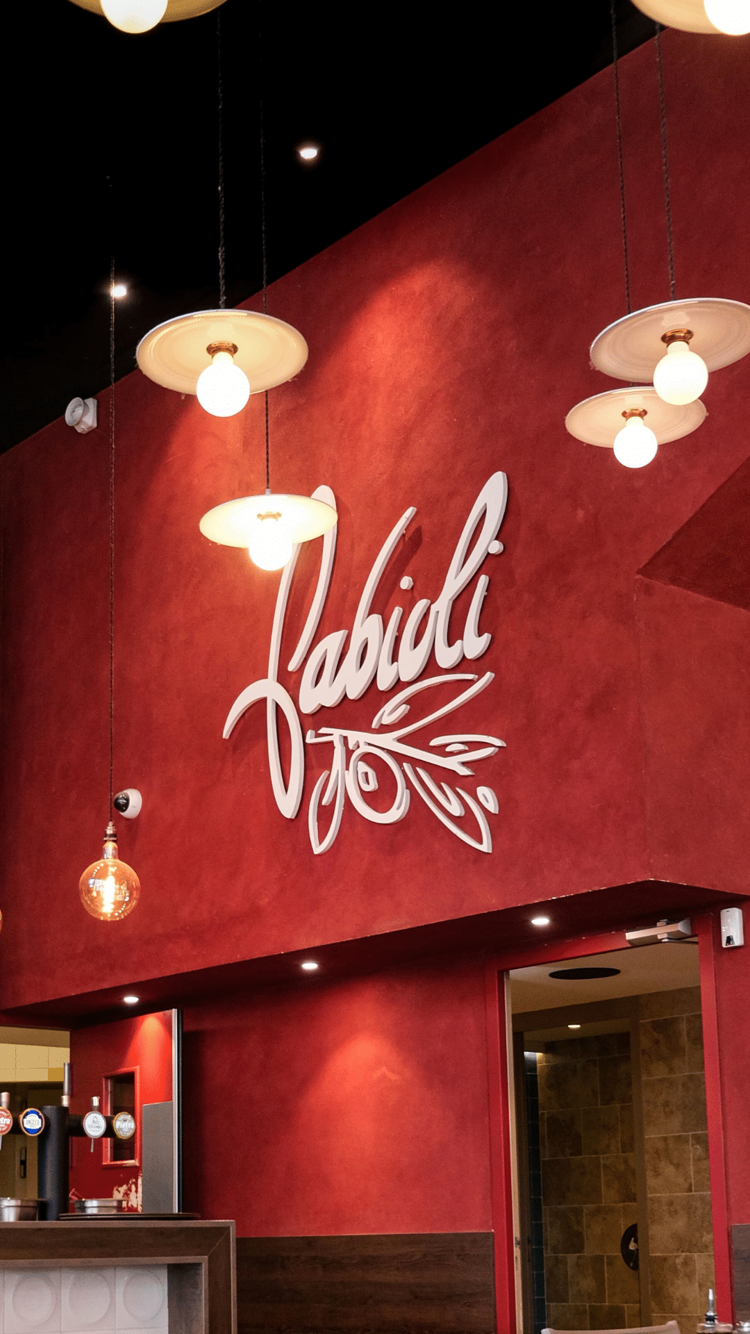 Salle du restaurant Fabioli avec son mur rouge, le grand logo blanc et les suspensions