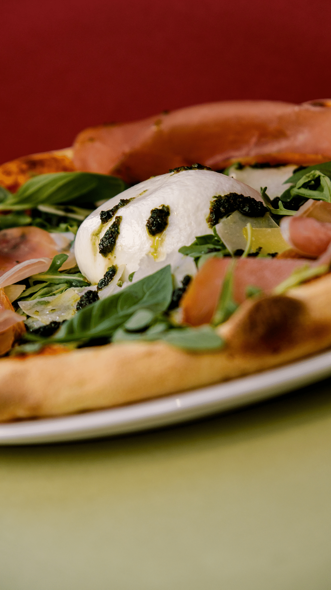Pizza burrata, pesto, jambon et roquette sur fond rouge