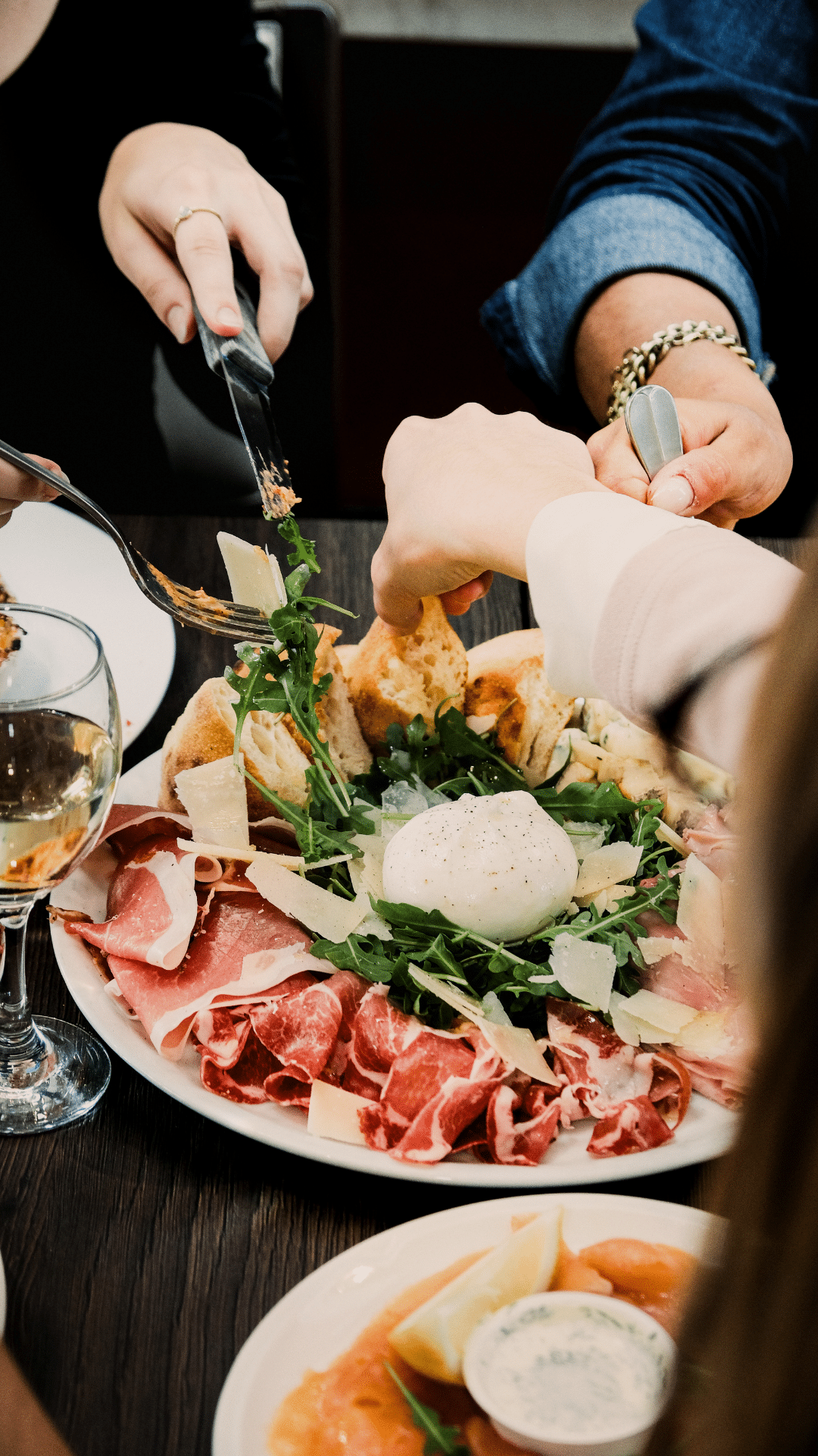Convives partageant une grande assiette d'antipasti avec burrata, jambon cru et roquette