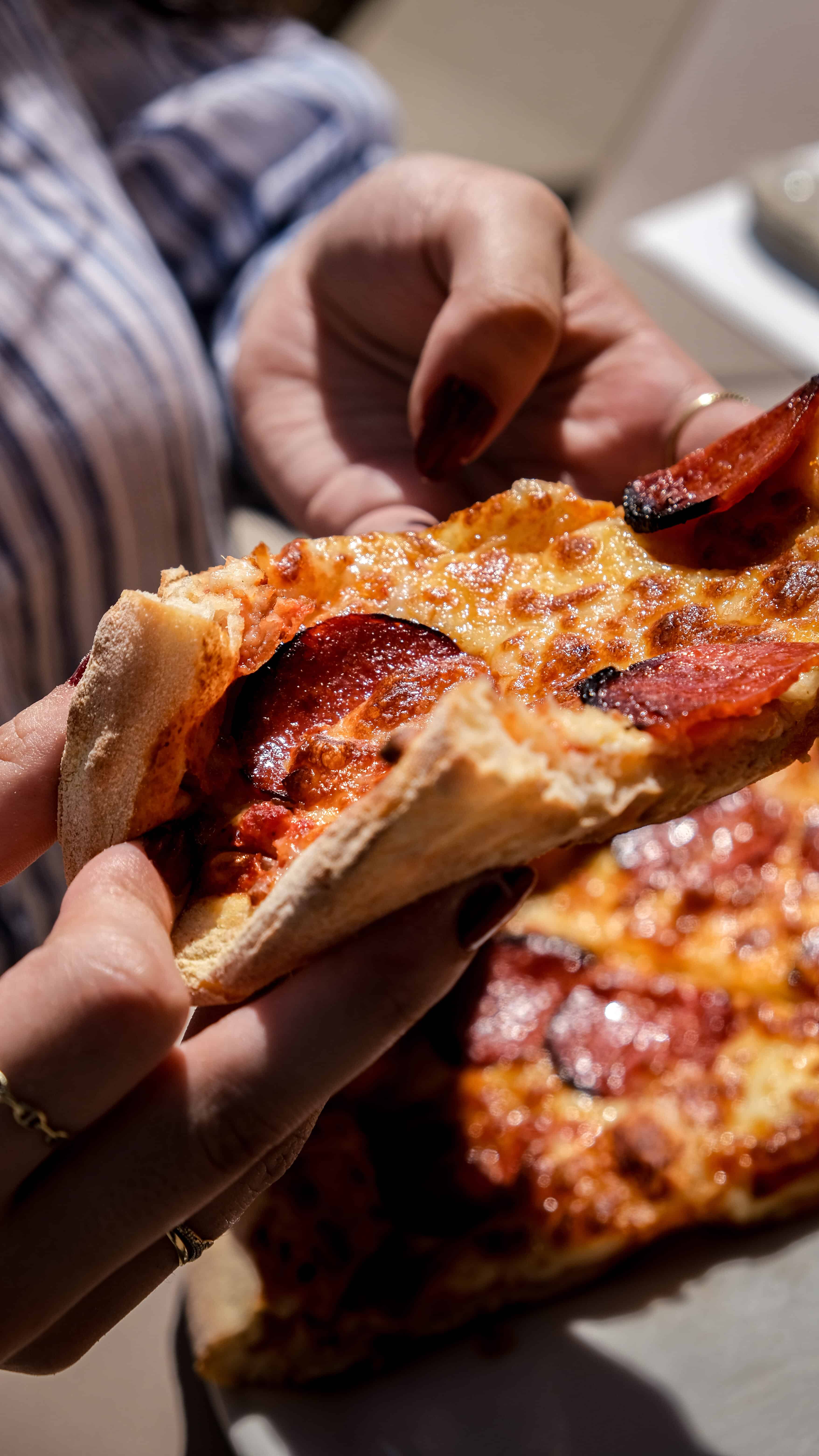 Deux parts de pizza pepperoni Fabioli partagées à la main au soleil