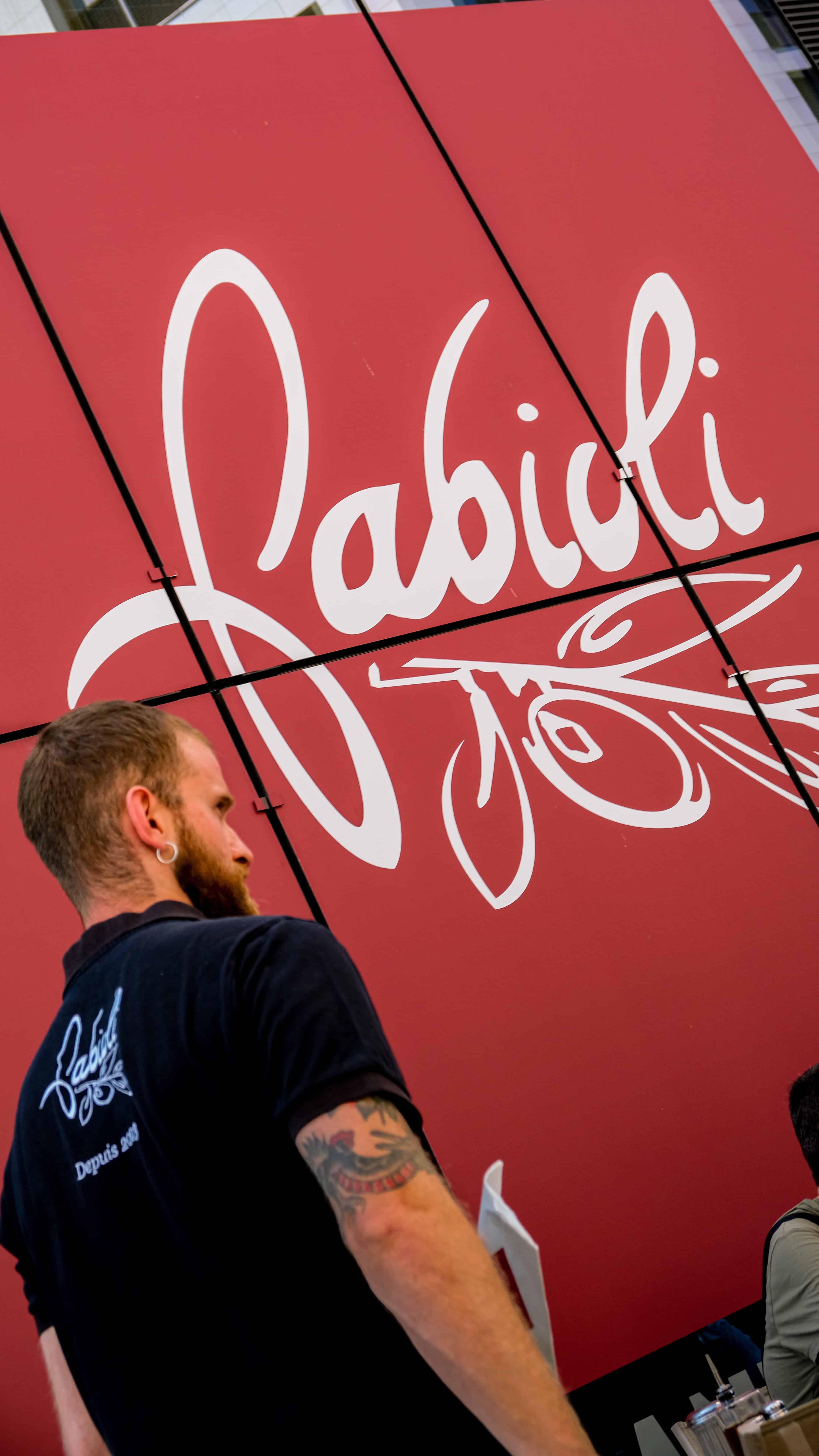 Membre de l'équipe Fabioli devant le grand logo mural de la marque