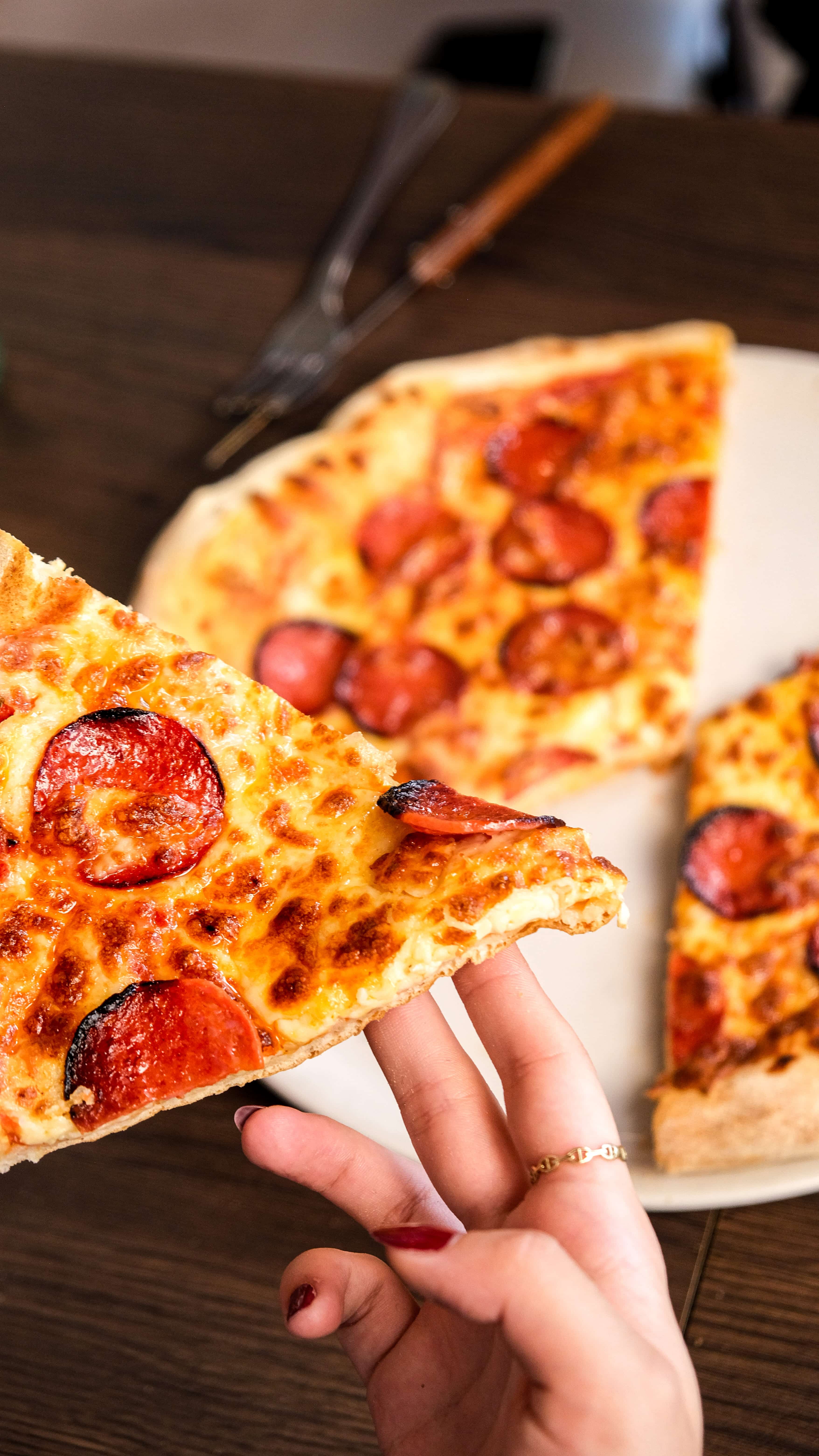 Part de pizza Fabioli au pepperoni tenue à la main, pâte fine et croustillante